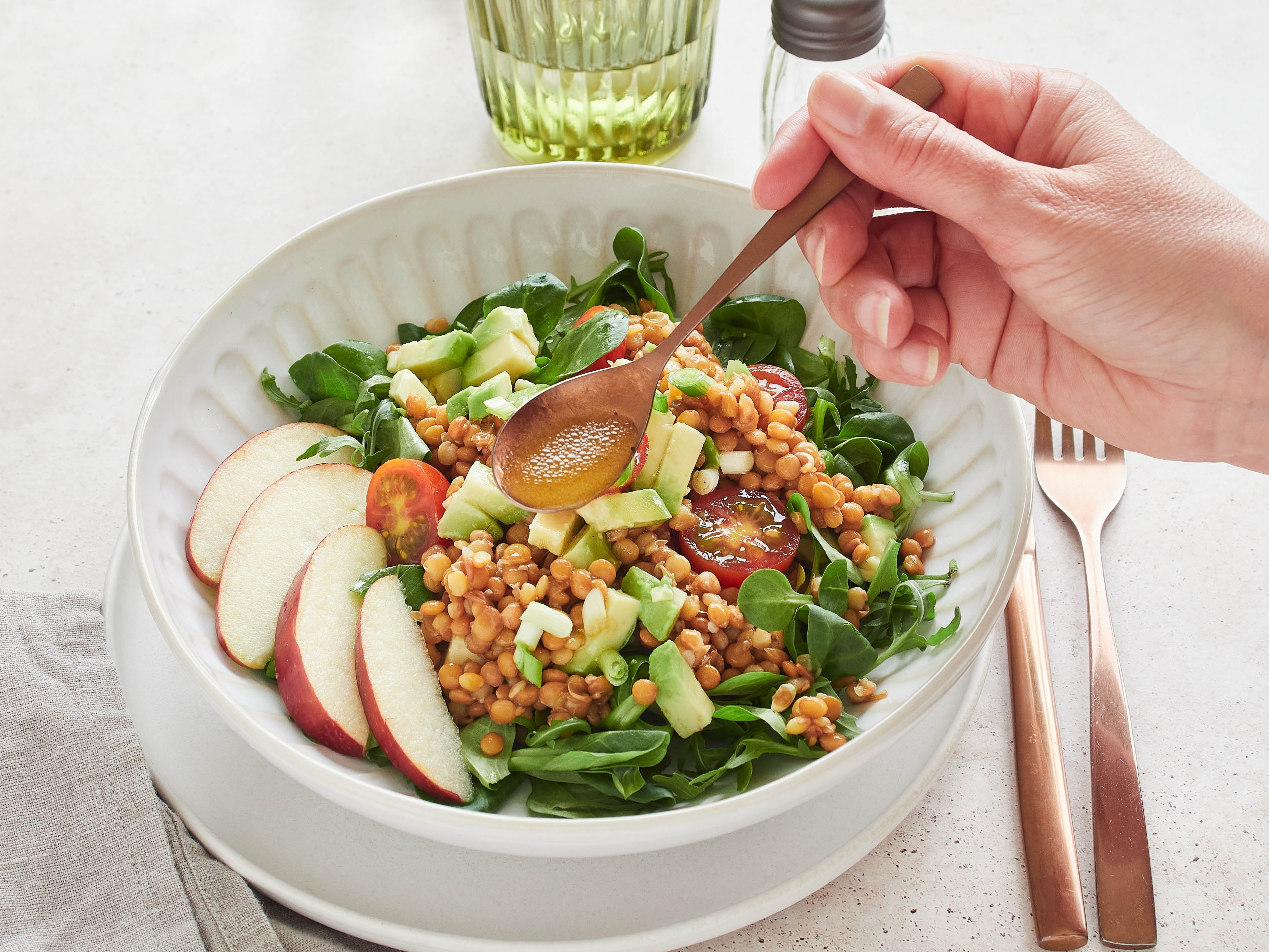 Close-up of person making a healthy salad for lunch that includes apples, veggies, and light dressing